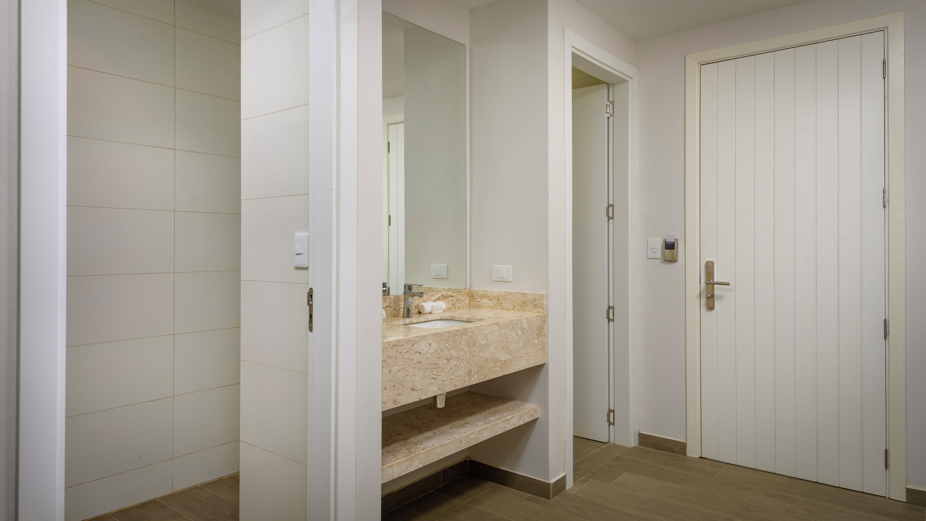 Un baño con lavamanos de m ármol, un espejo y una puerta blanca.