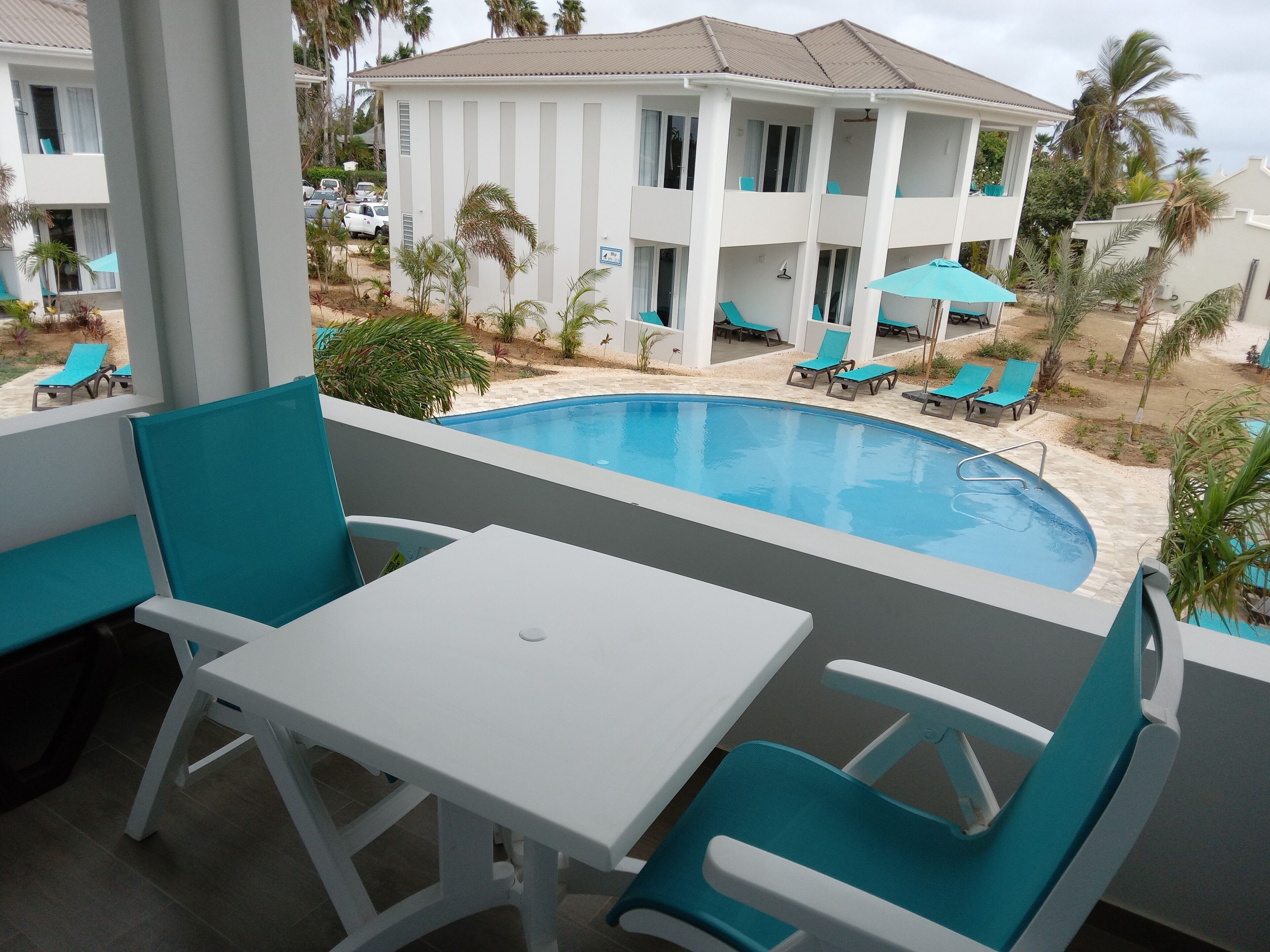 A poolside area with a white table and chairs, a pool, and a building with balconies in the background.
