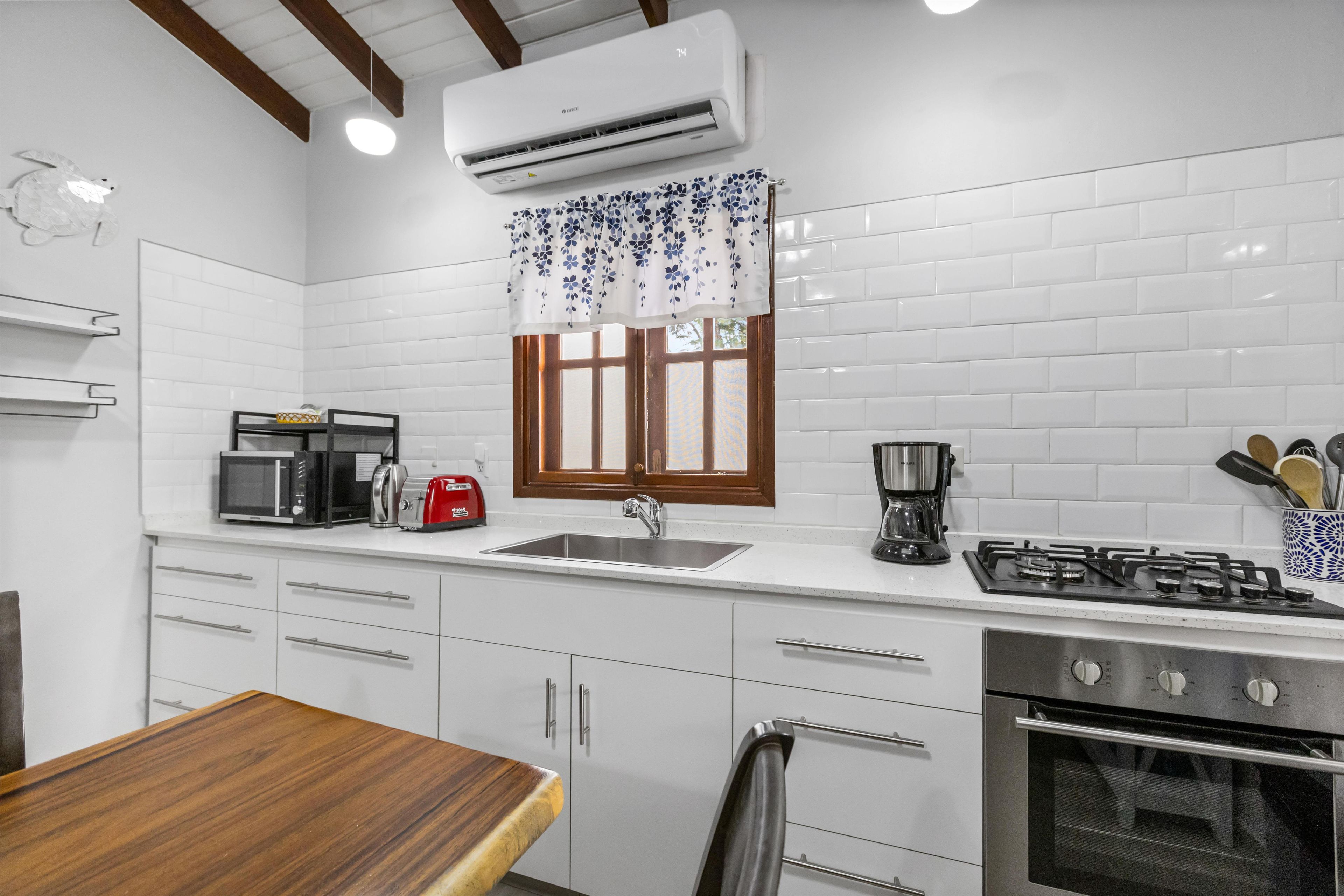 A modern kitchen with white tiles, a gas stove, a microwave, a toaster, and a sink.