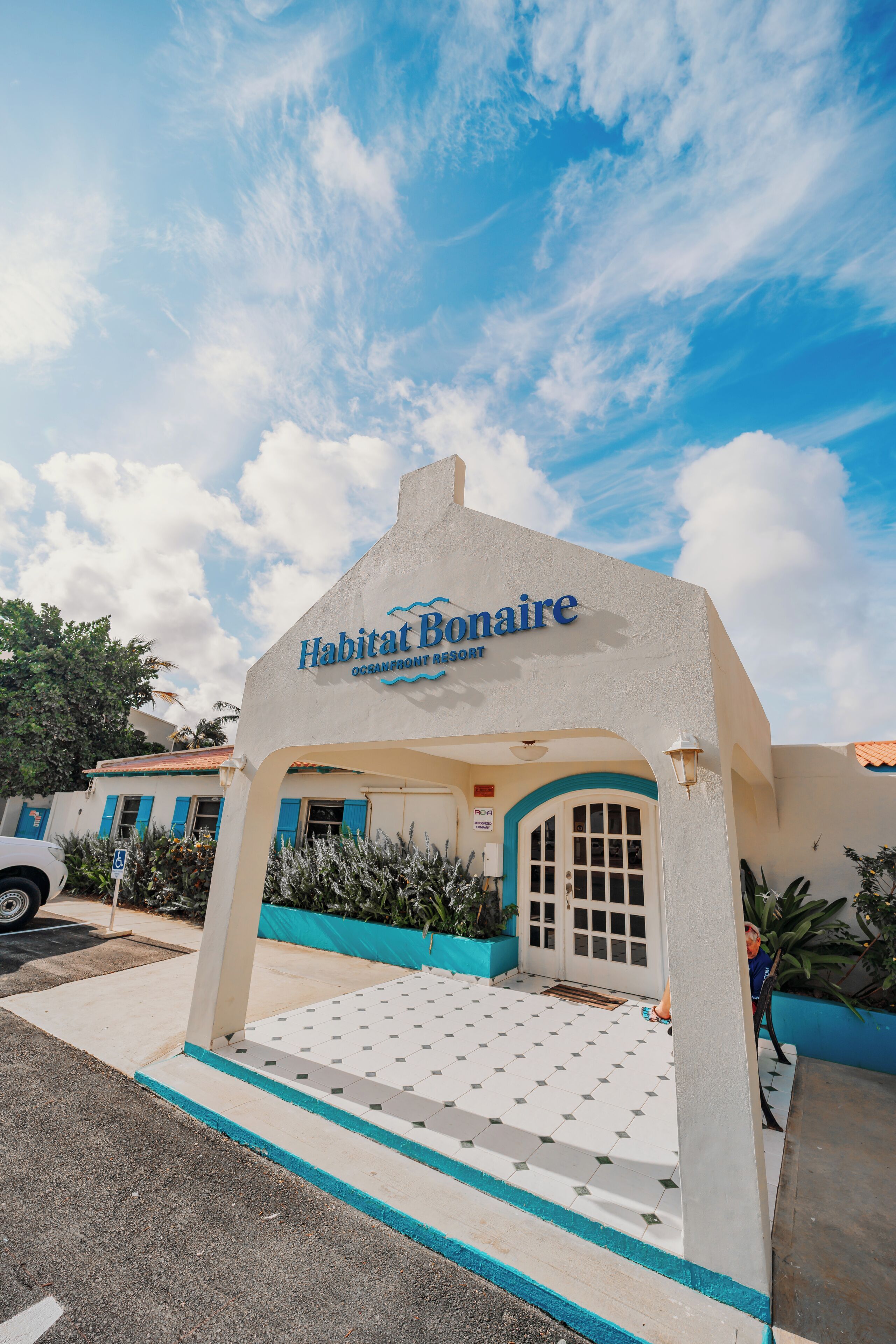 A building with a sign reading "Habitat Bonaire." It has a white facade, blue trim, and a tiled entrance.