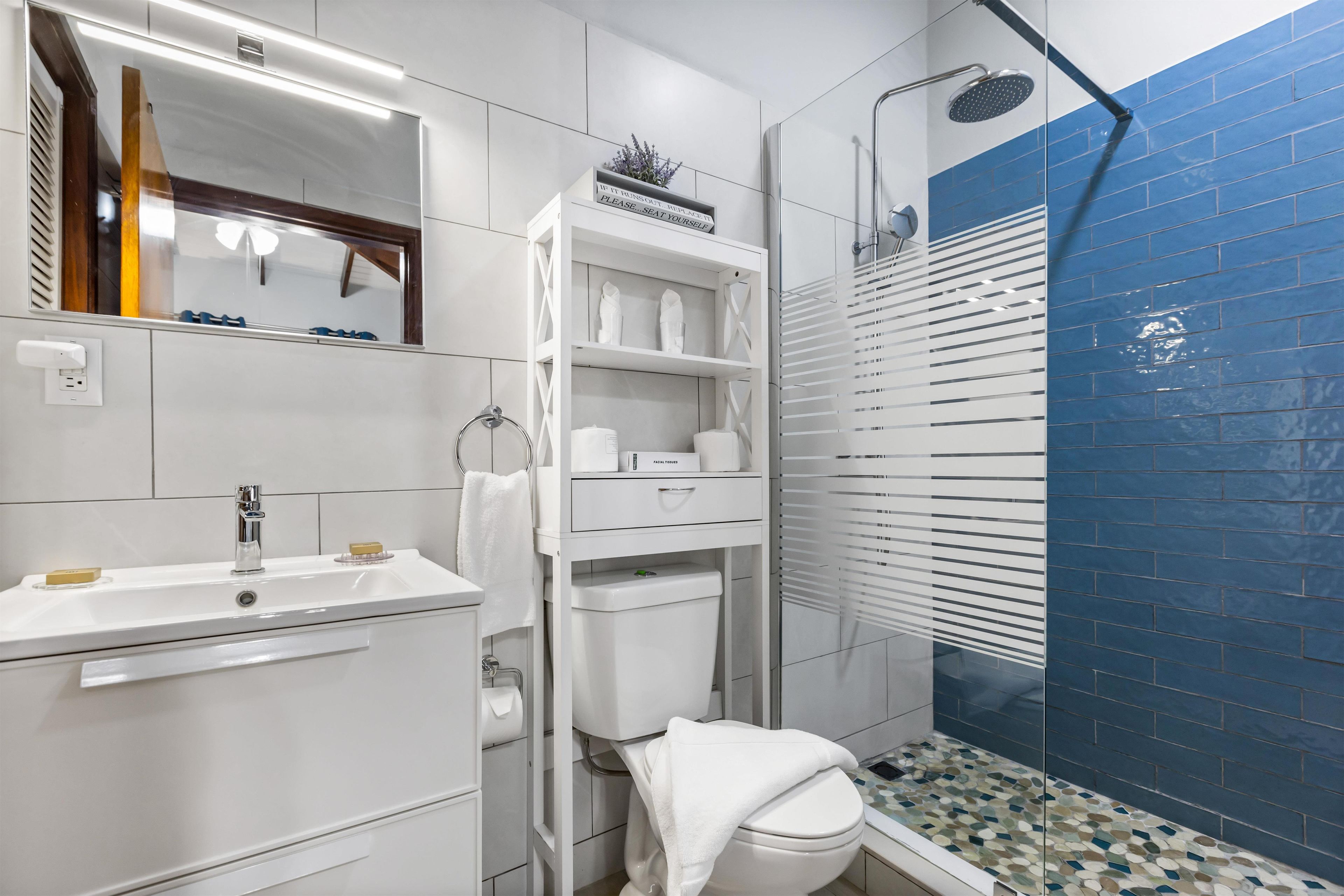 Un baño moderno con lavamanos, inodoro y zona de ducha blancos.