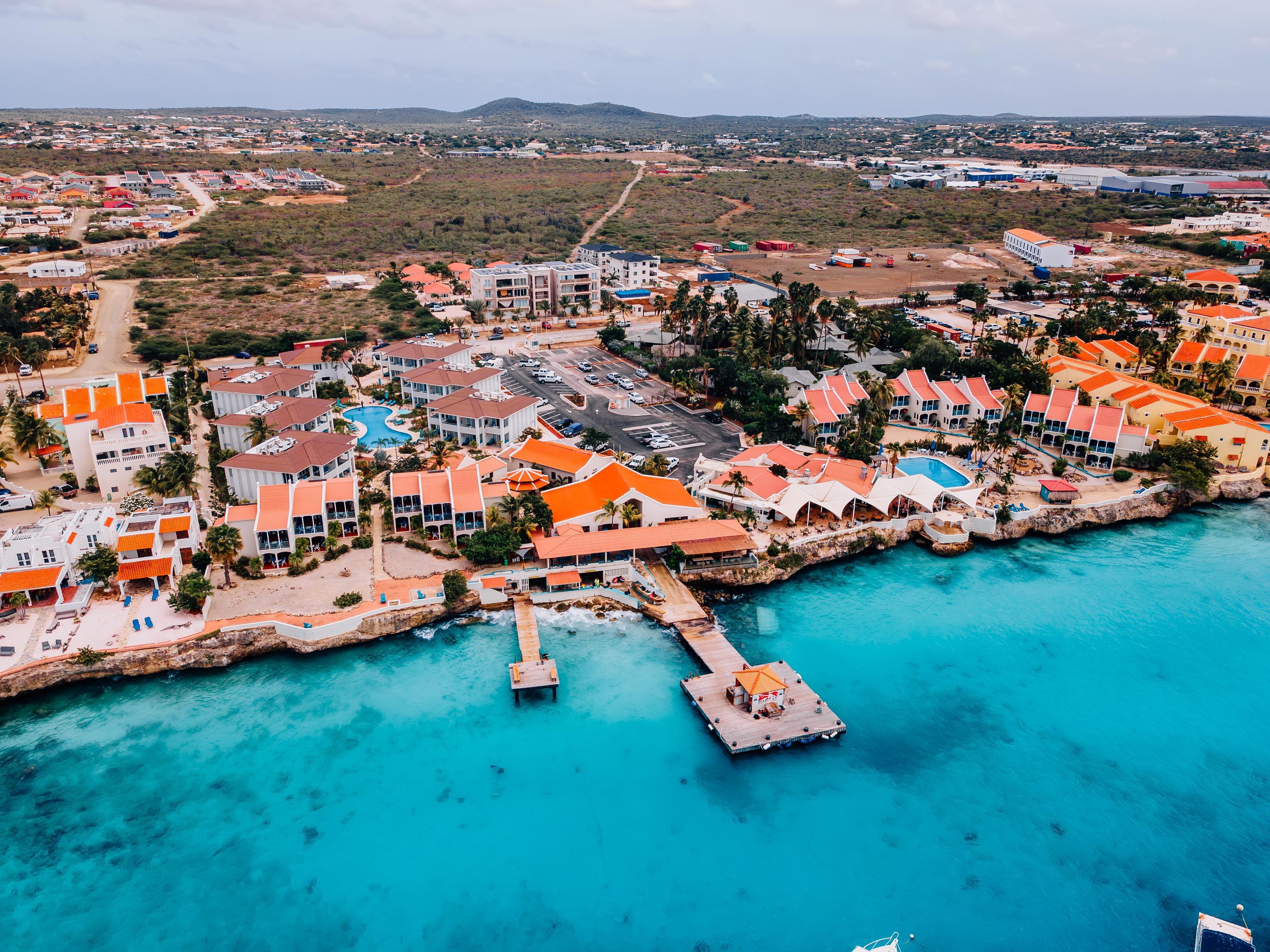 A coastal resort with multiple buildings, a swimming pool, and a pier extending into the turquoise sea.