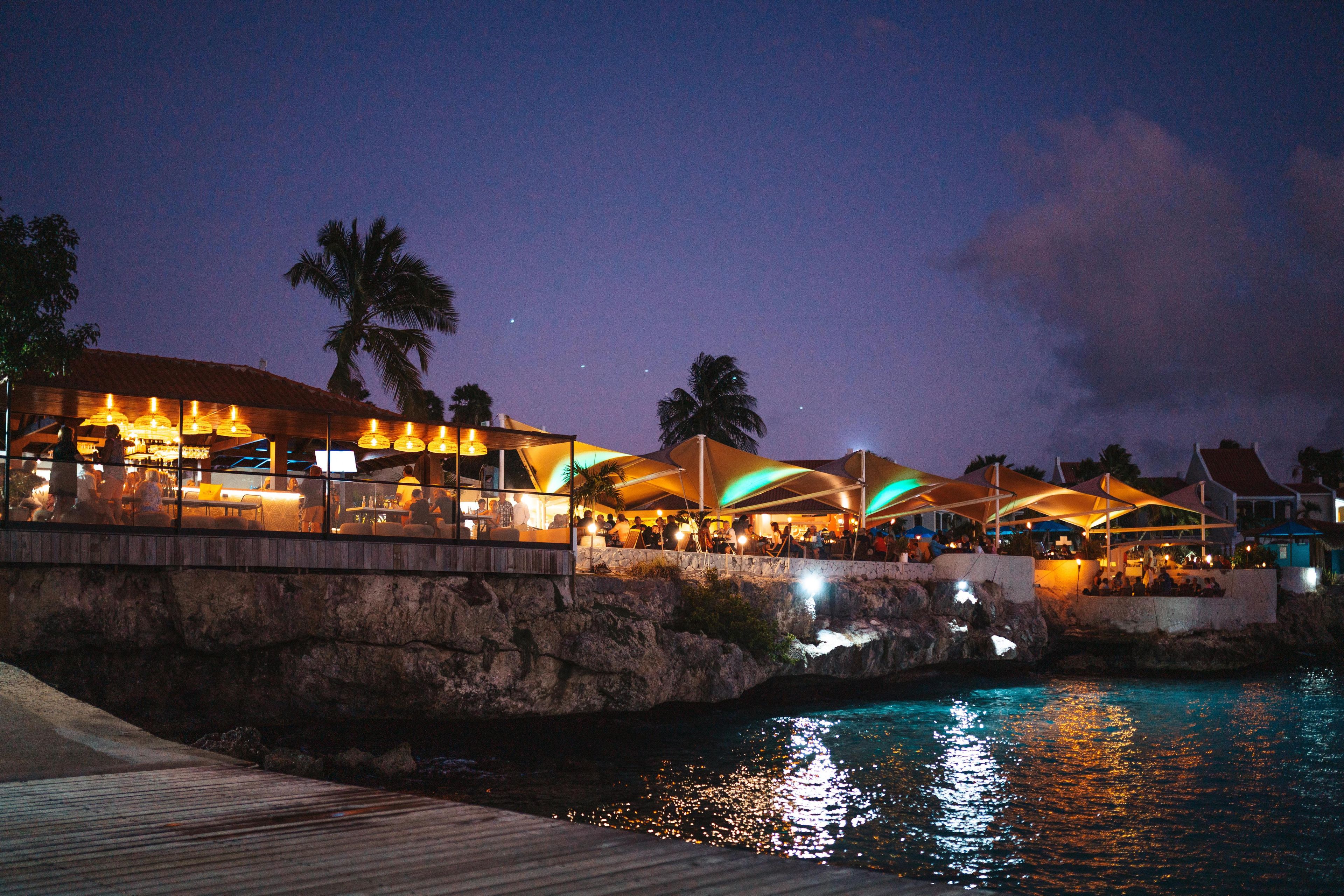 A waterfront restaurant with outdoor seating and a pool.