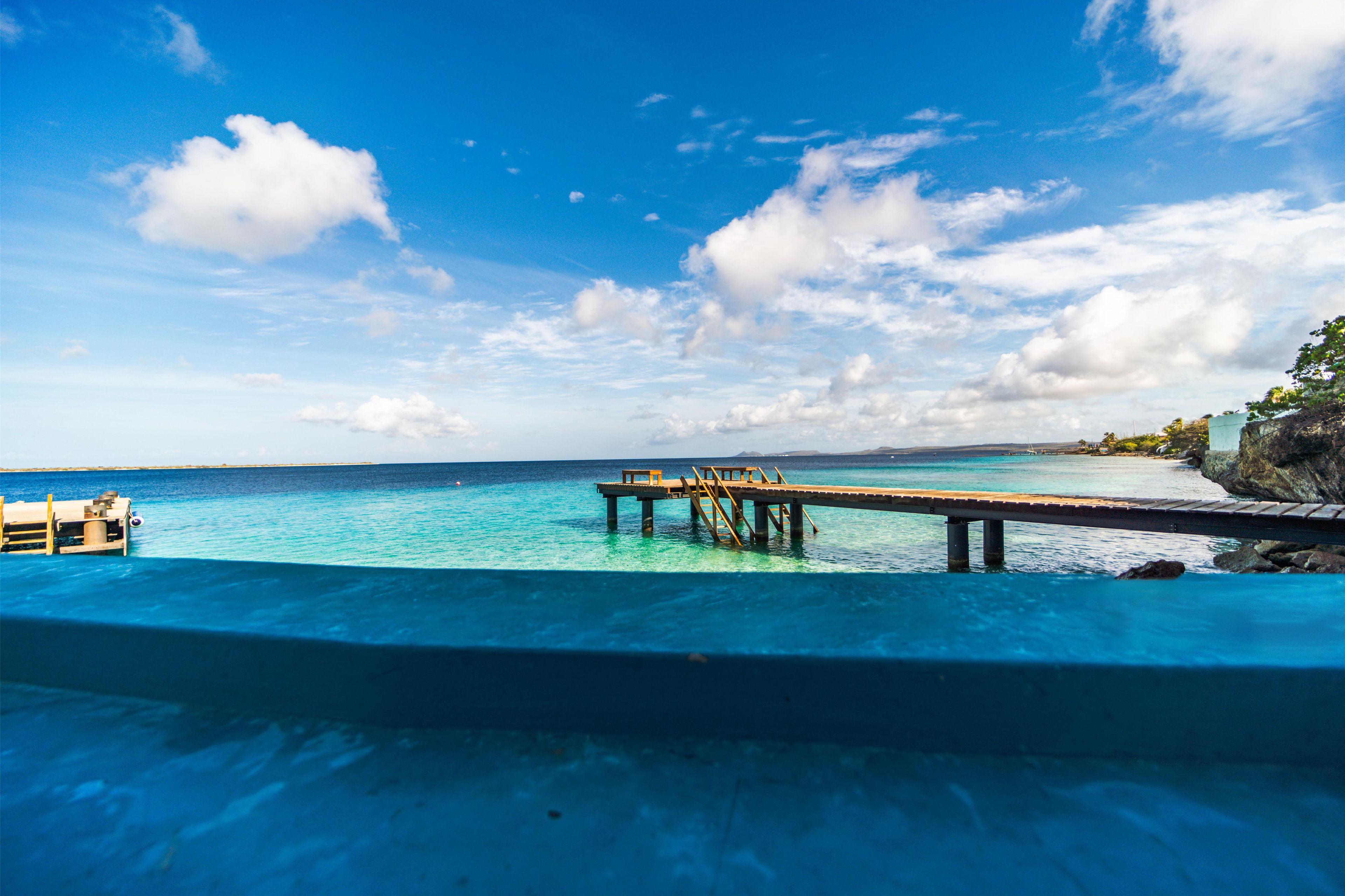A clear blue sky with a wooden pier extending into the turquoise sea.