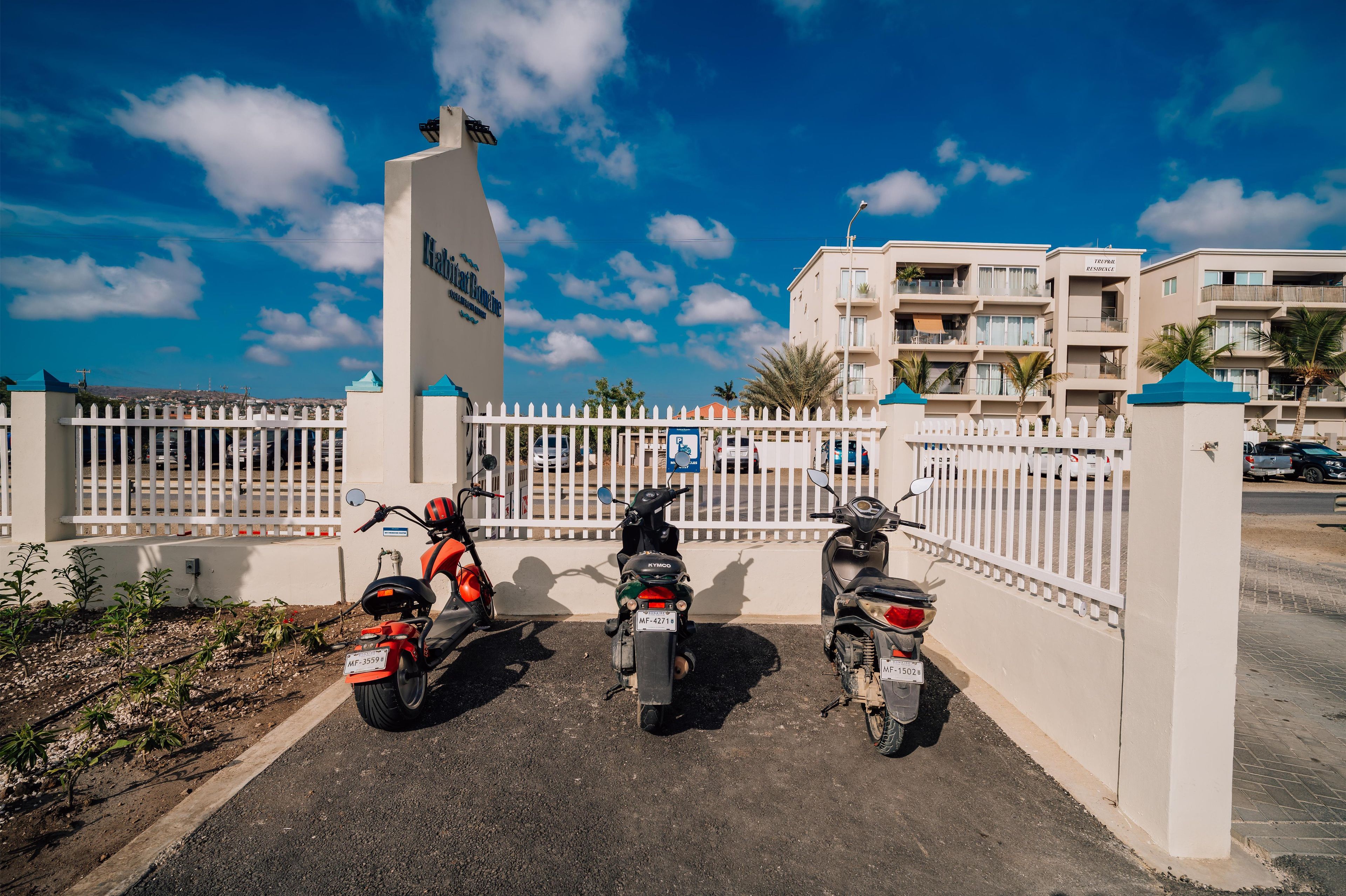 A gated parking area with three motorcycles parked in front of a building with a sign that reads 'Hotel Romane'.