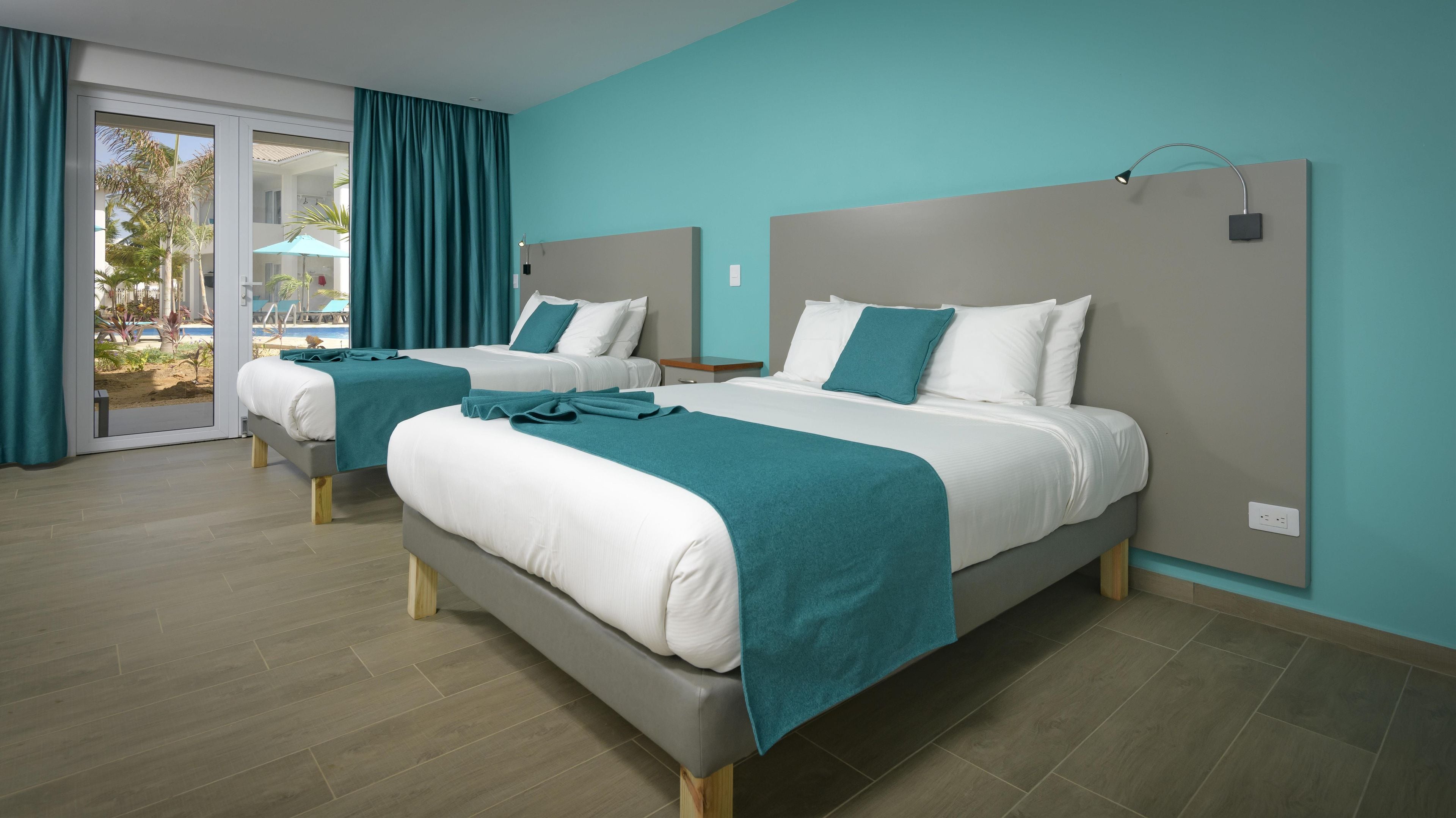 A hotel room with two beds, a sliding glass door to a pool area, and a teal color scheme.