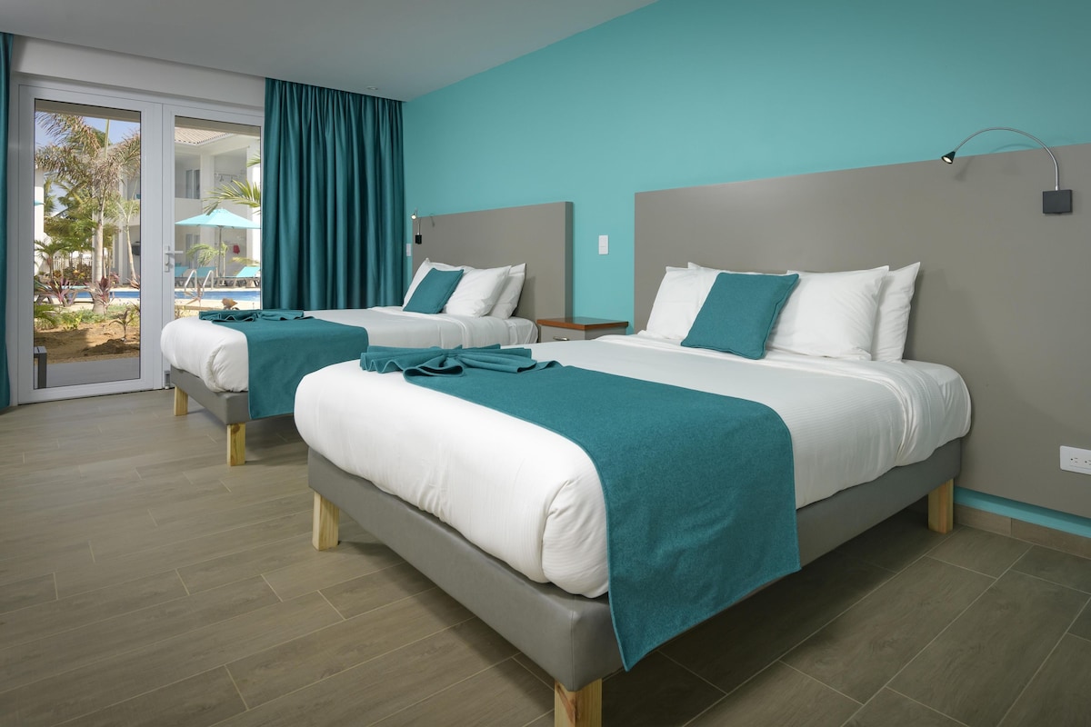 A hotel room with two beds, a sliding glass door to a pool area, and a teal color scheme.