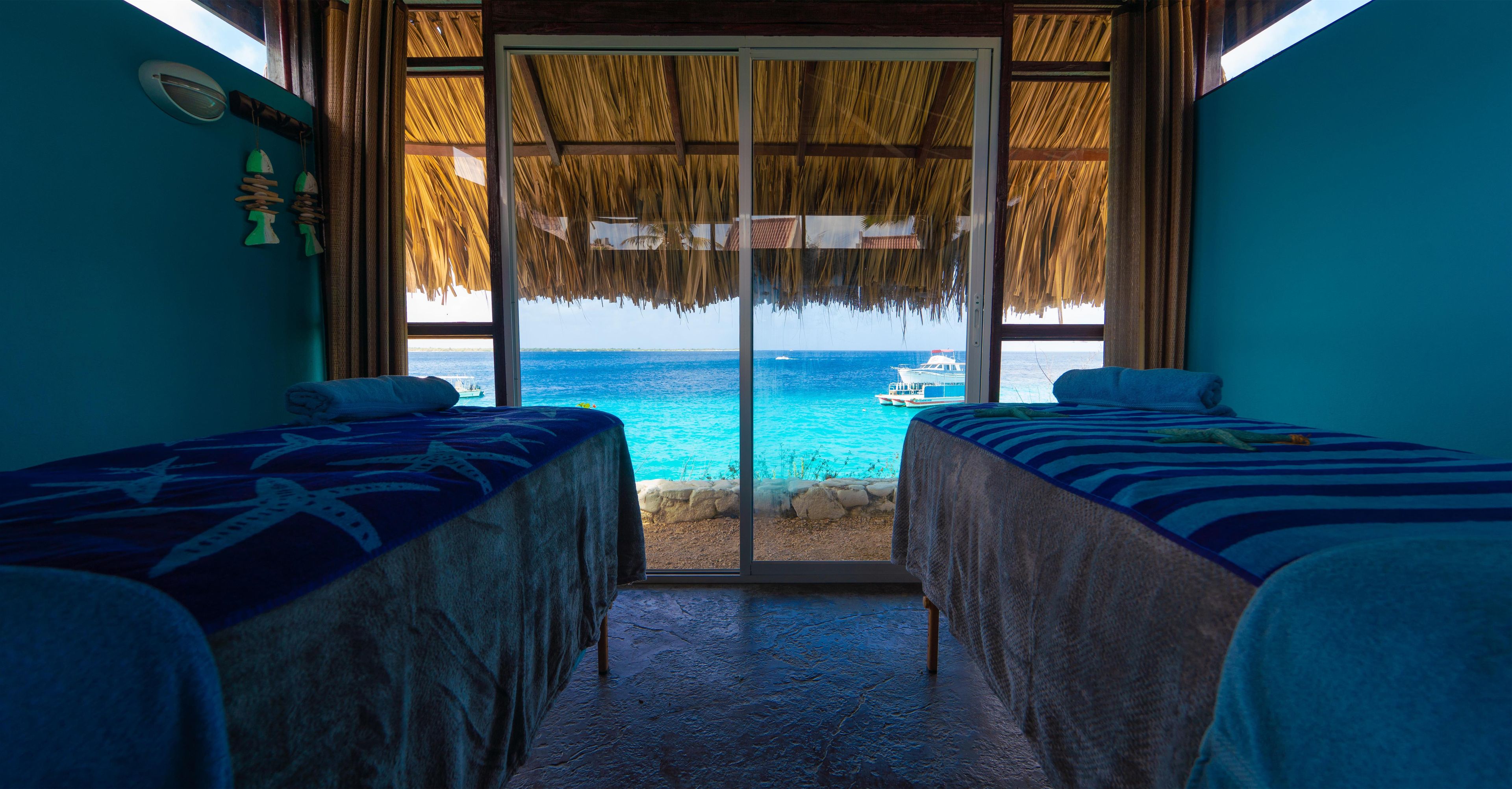 A room with two beds, a view of the sea, and a boat in the distance.