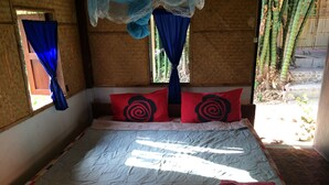 A bed with a patterned bedspread, two red pillows with a black design, and a blue curtain. - Rainbow House (Pai)