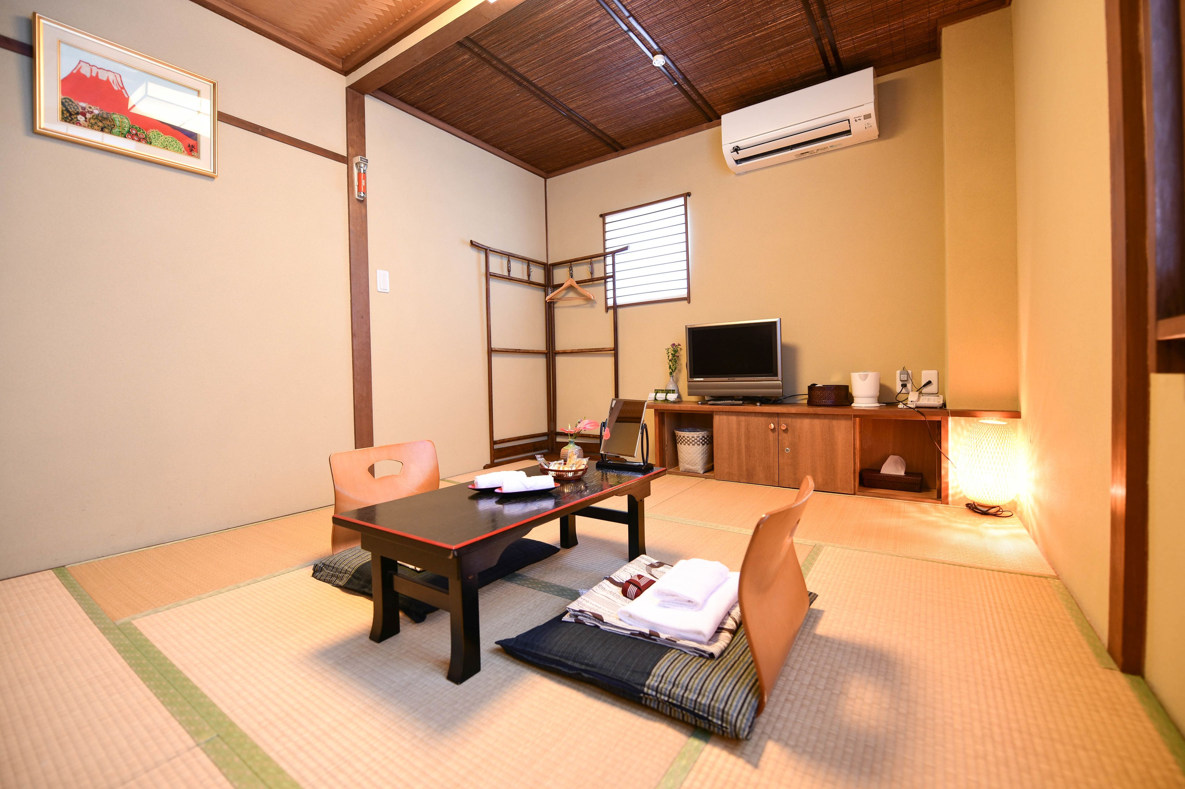 A traditional Japanese room with tatami flooring, a low table, a sofa, a TV, and a hanging clothes rack.