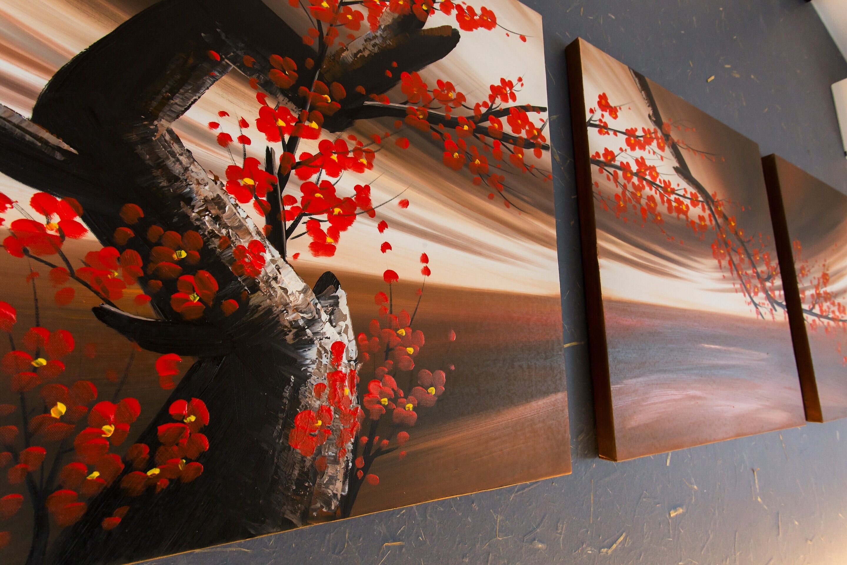 A wall with three framed paintings of a tree with red flowers.