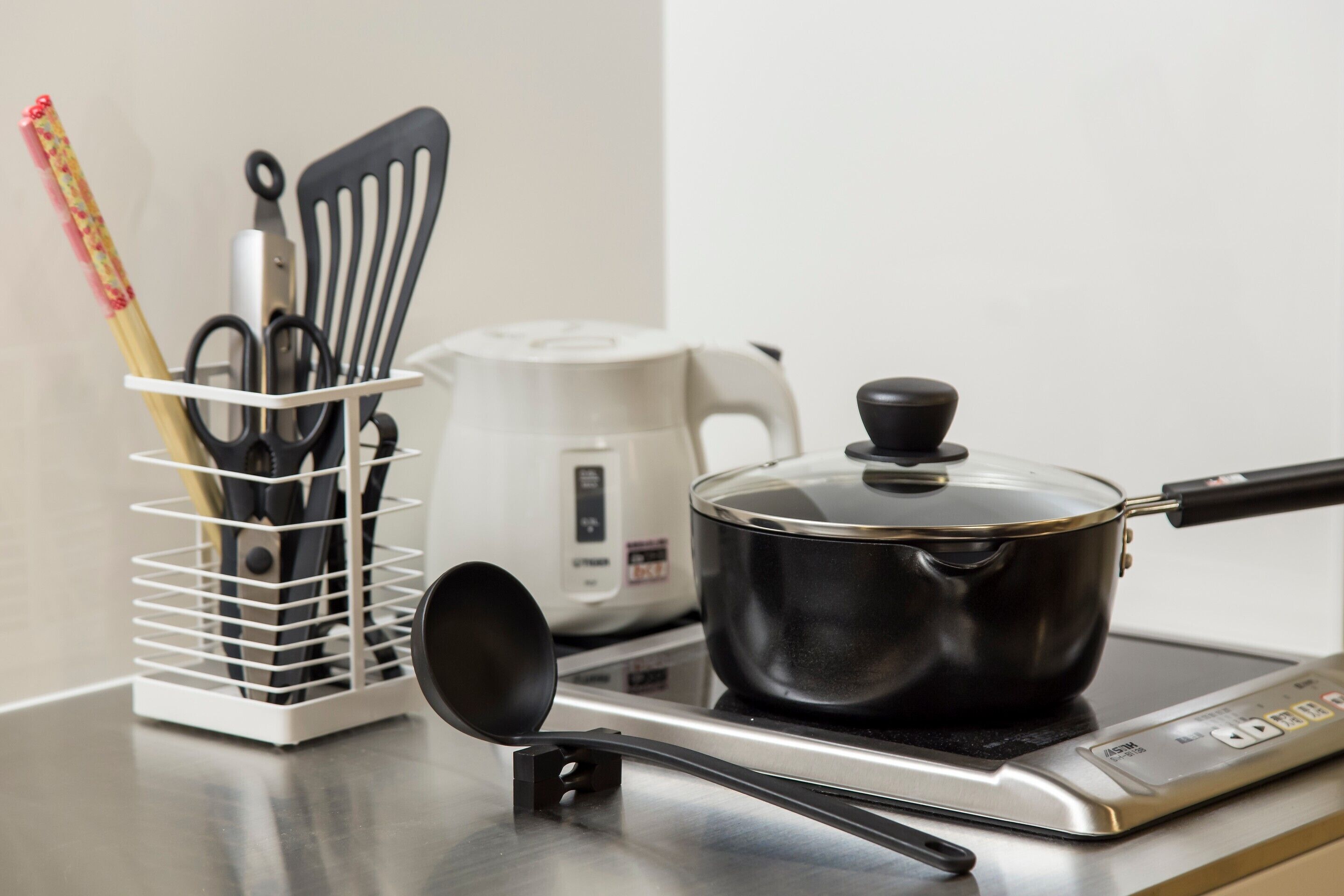 A kitchen with a stove, a pot, a kettle, and a utensil holder.