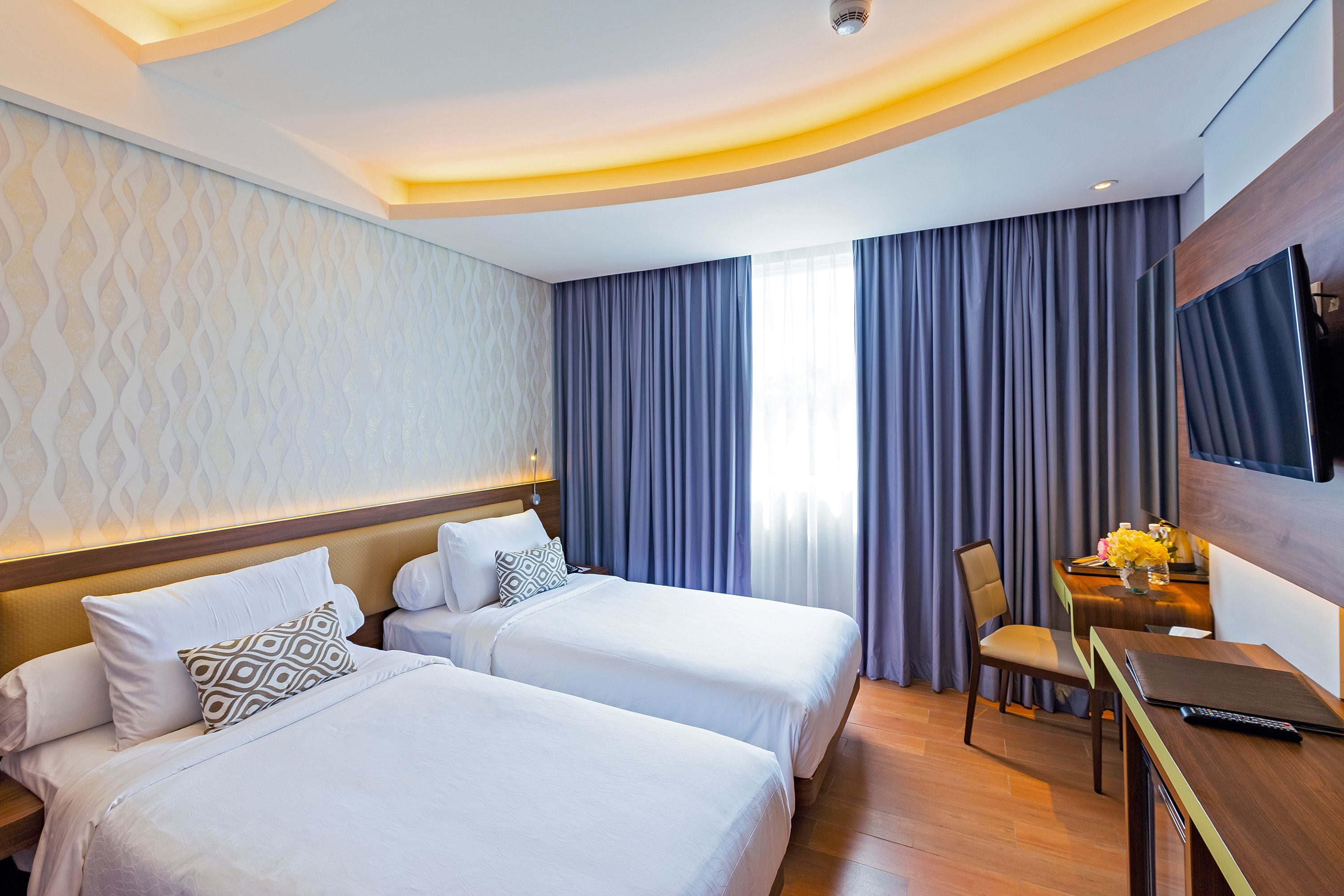 A hotel room with two beds, a desk with a chair, a TV, and a window with curtains.