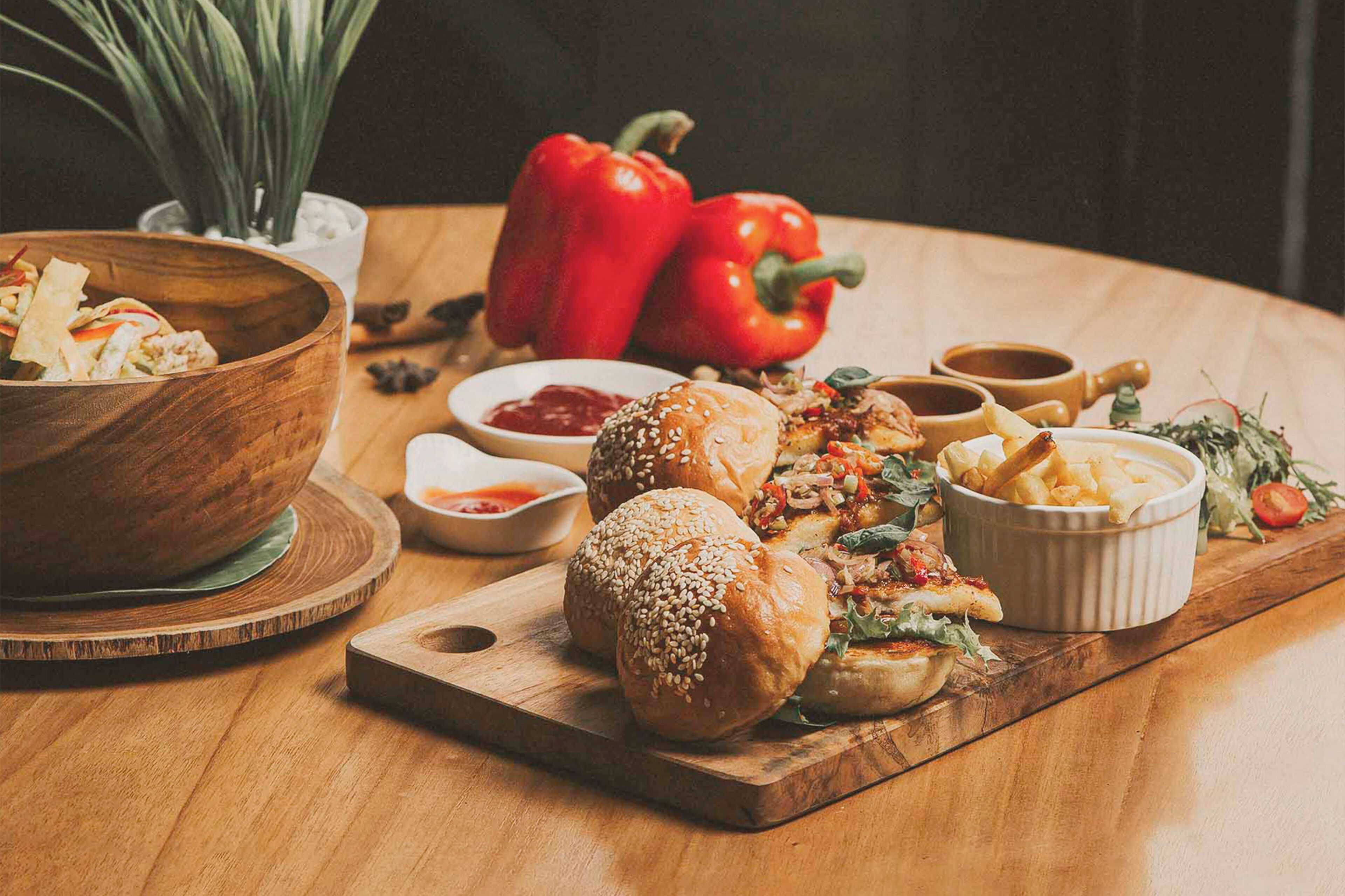 Une table en bois sur laquelle on trouve divers aliments, notamment des petits pains, un saladier rempli de salade et un plat de frites.