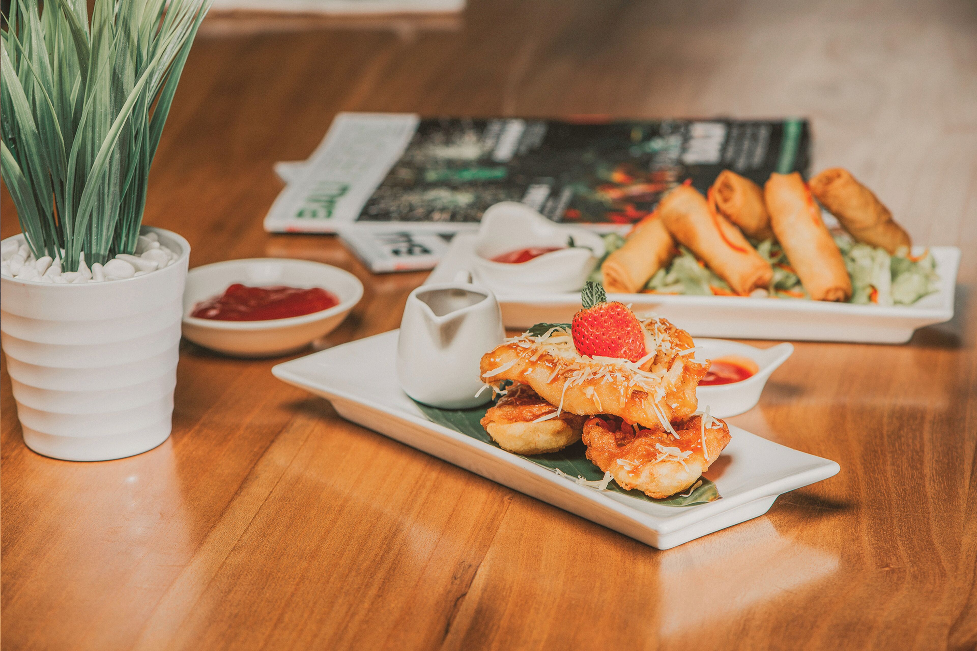 A dining table with a variety of dishes, including spring rolls, a bowl of sauce, and a small pitcher.