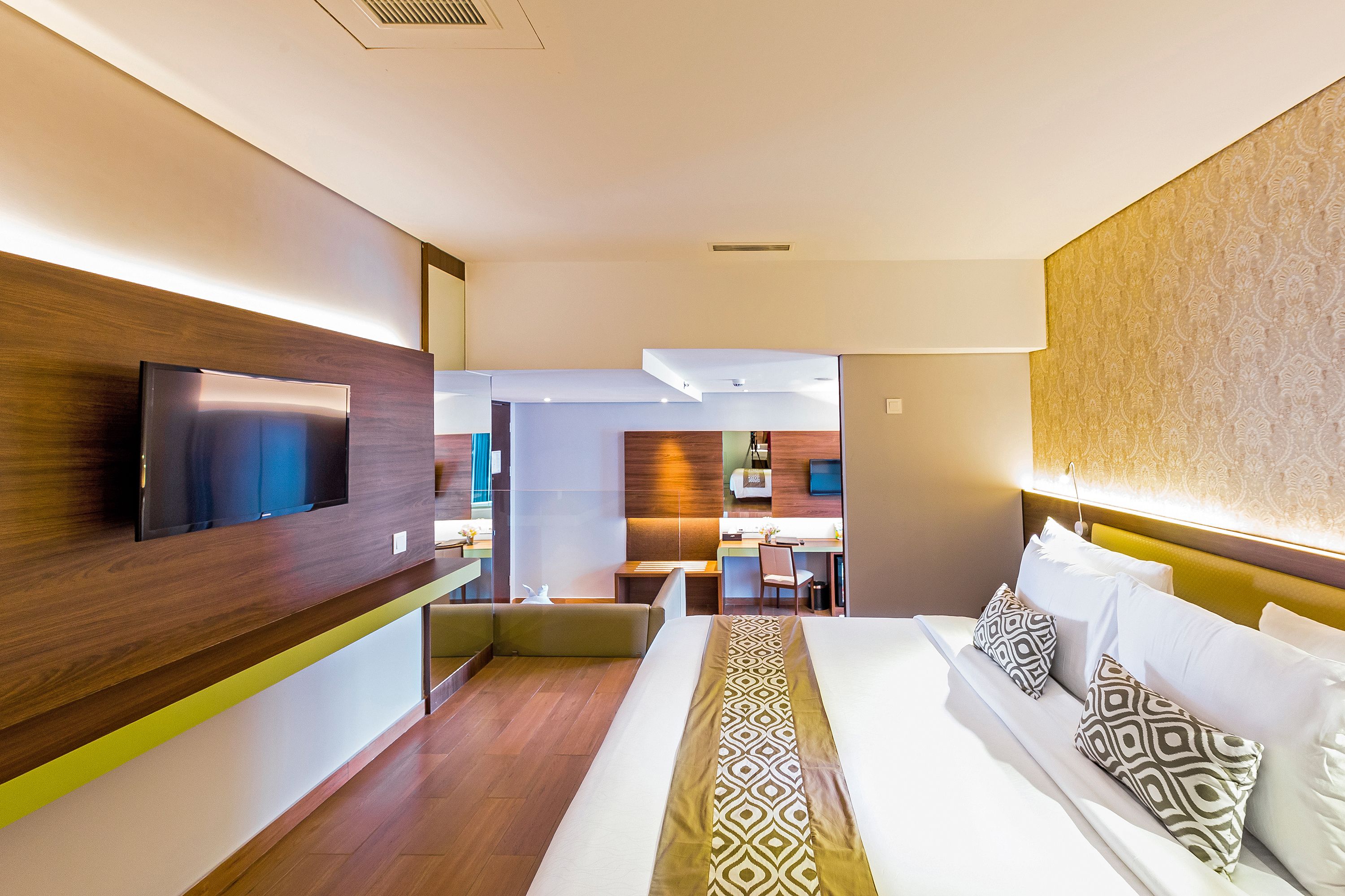 A modern hotel room with a large bed, a flat-screen TV mounted on the wall, and a small seating area with a table and chairs.