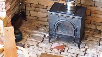 A stone fireplace with a black stove, a wooden chair, and a small table in front of it.