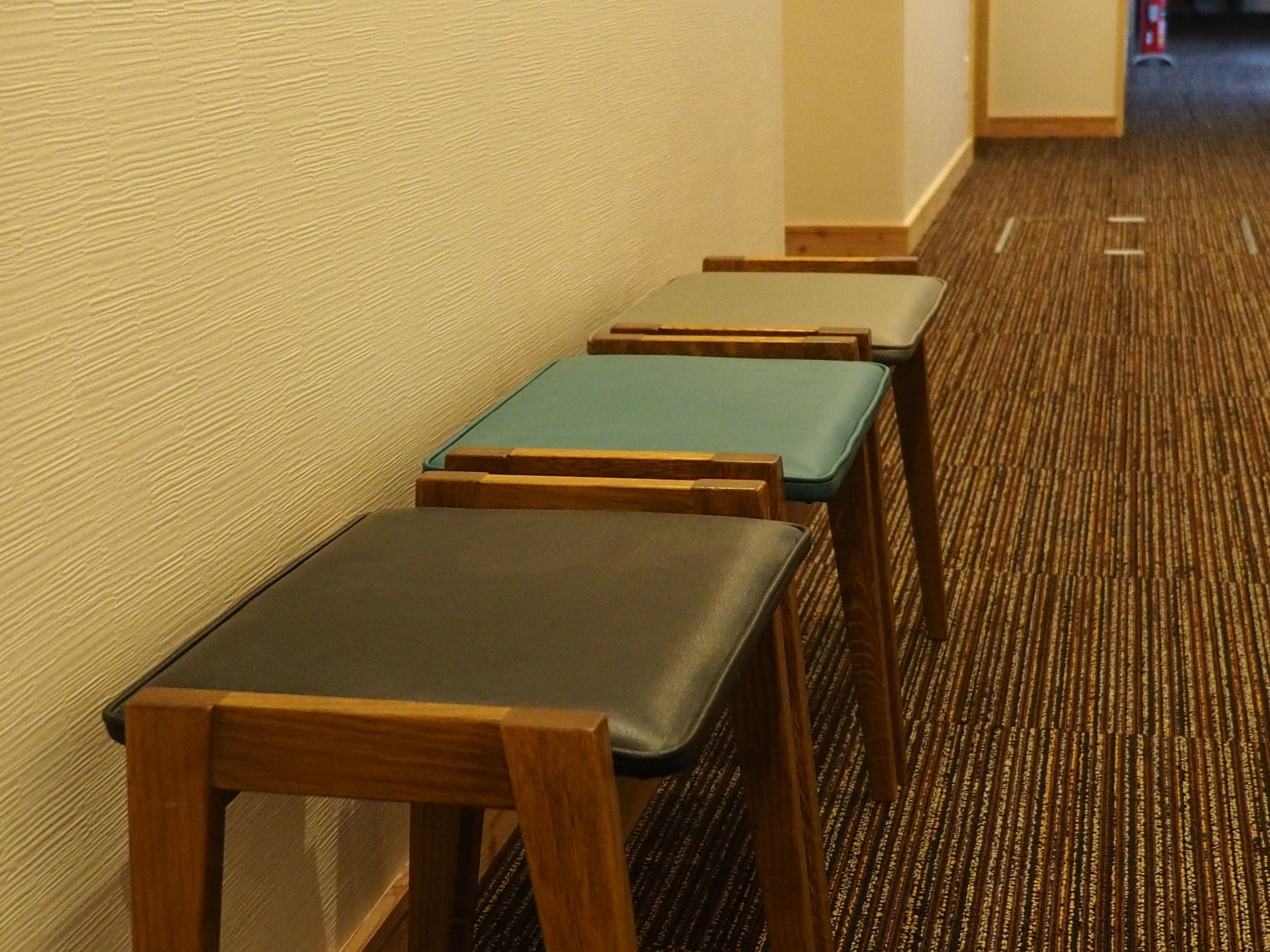 A hotel corridor with wooden chairs and tables arranged in a row.
