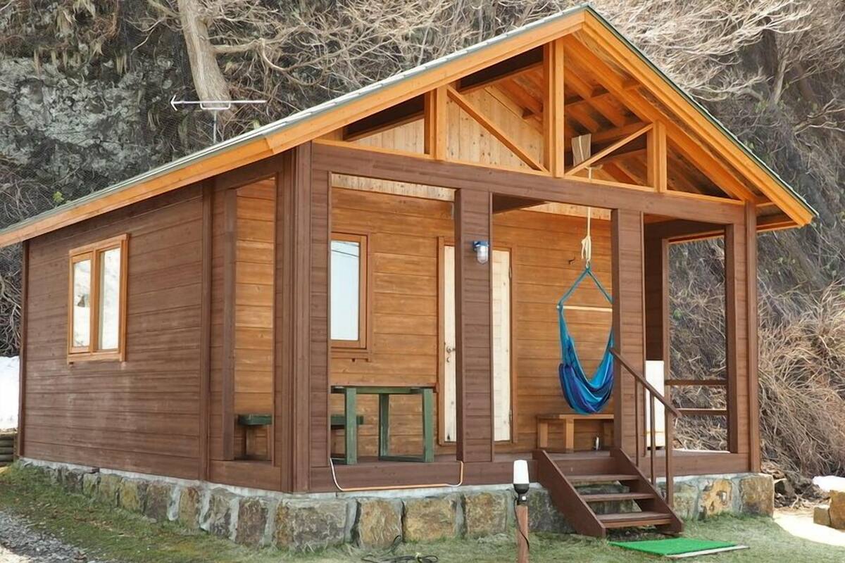 A wooden cabin with a porch, a hammock, and a staircase leading to the entrance.