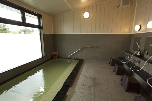 Una piscina con plataforma de azulejos, un banco de madera y zona de ducha con mampara de vidrio.
