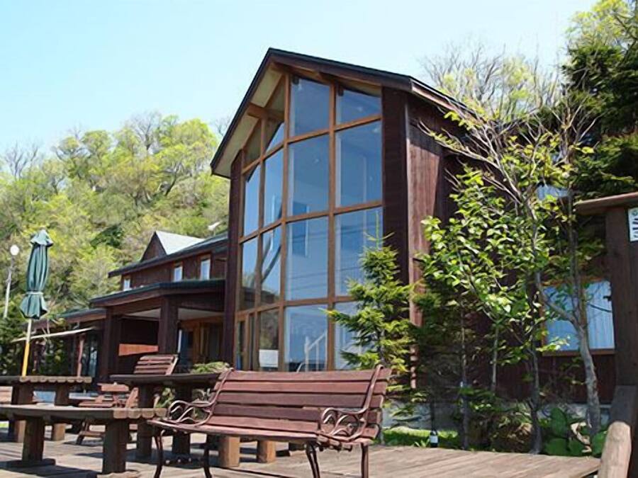 Una cabaña de madera con amplias ventanas, una terraza y asientos exteriores.