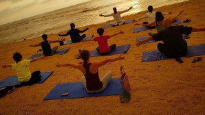 Un groupe de personnes pratiquant le yoga sur des tapis, sur une plage, avec l’océan en arrière-plan.