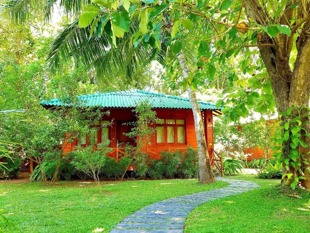 Una casa de madera roja con techo verde, rodeada de abundante vegetación y un sendero de piedra.