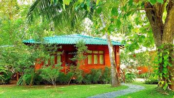 Una casa de madera roja con techo verde, rodeada de abundante vegetación y un sendero de piedra.