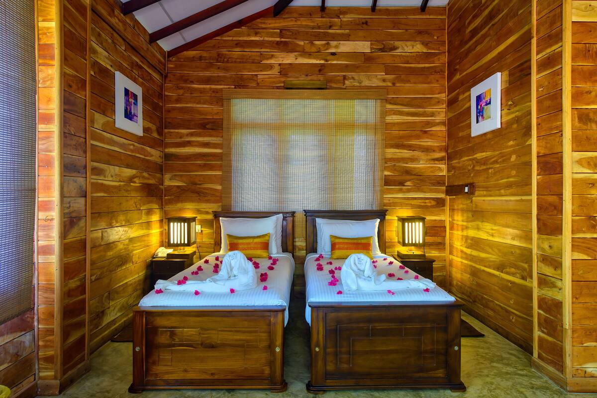 Une chambre dans un chalet en bois, avec deux lits, chacun doté d’une table de chevet et d’une lampe.