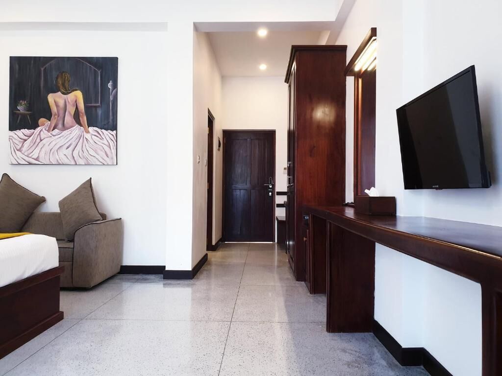 Habitación de hotel con cama, sofá, televisión, un cuadro y un armario de madera.
