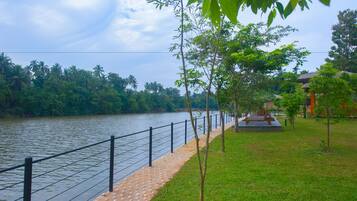 Un paseo junto al río con valla, árboles y una pequeña zona de parque.