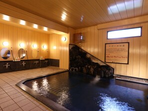 Een traditioneel Japans onsen met houten wanden, een stenen warmwaterbron en meerdere wasbakken met spiegels.