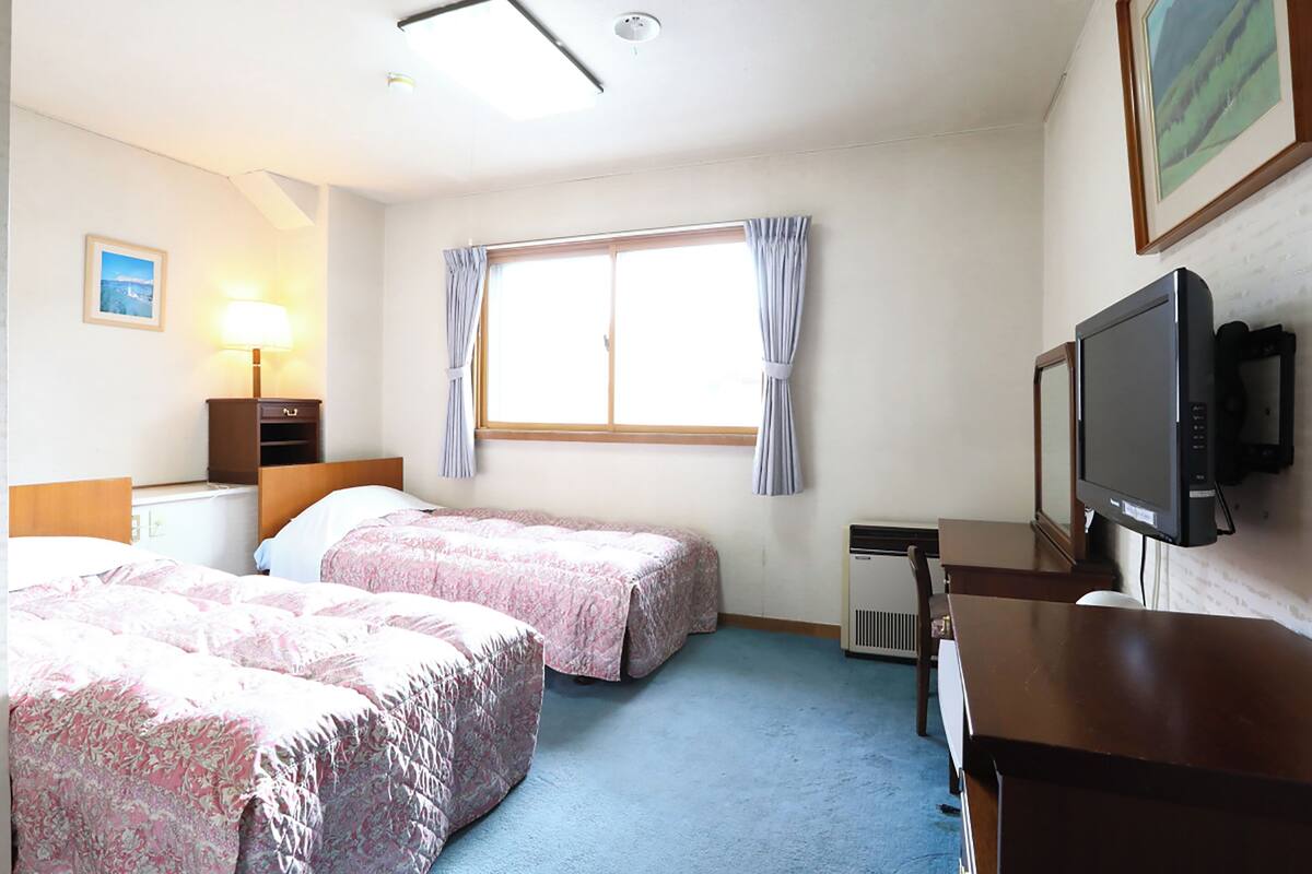 Une chambre d’hôtel avec deux lits, un bureau, une télévision et une fenêtre avec des rideaux.