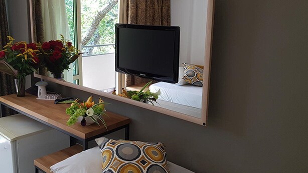 A hotel room with a bed, a bedside table with a TV, a mirror, and a window with curtains. - Tintyava Park Hotel (Varna)