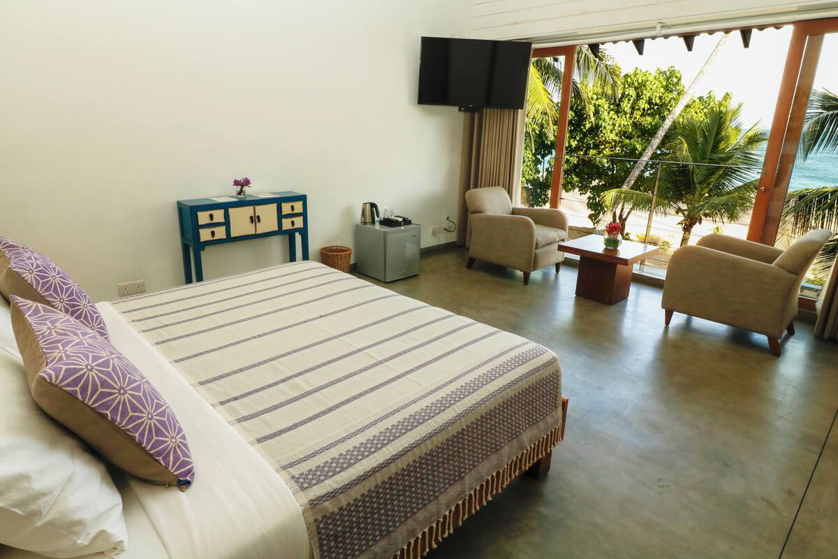 A hotel room with a bed, a small desk, a chair, a TV, and a view of the ocean.