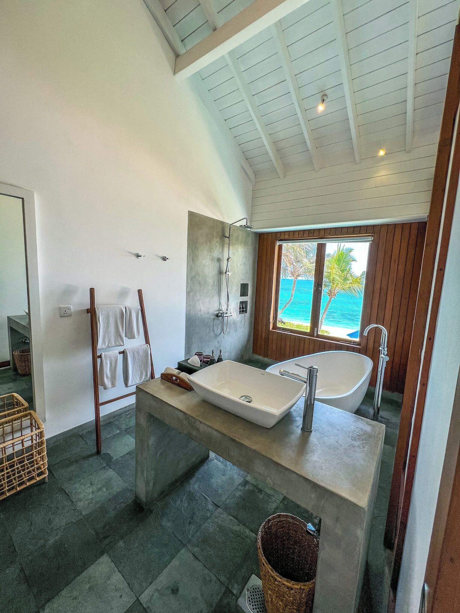 A modern bathroom with a freestanding bathtub, a large mirror, and a view of the ocean.