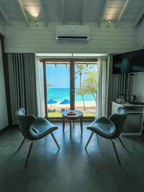Habitación con vista a la playa, dos sillas, una mesa y un televisor en la pared.