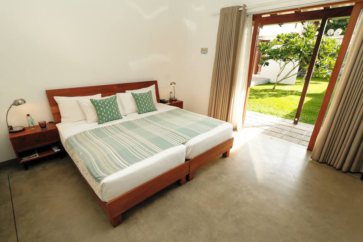 A bedroom with a large bed, wooden headboard, and a view of a garden through a sliding door.