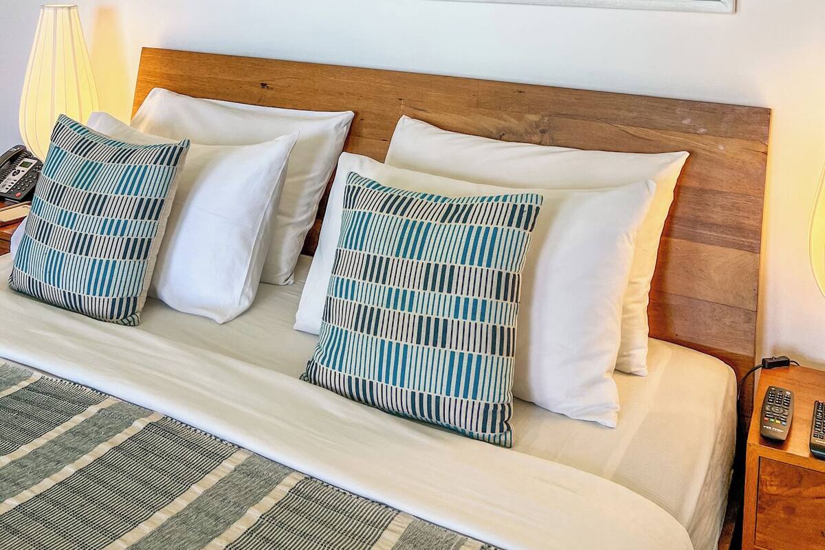 A neatly made bed with white and striped pillows, a wooden headboard, and two abstract paintings on the wall.