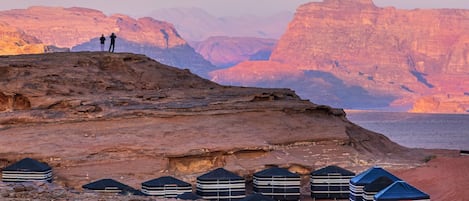 A rocky landscape with yurts and two people standing on a cliff overlooking a canyon.