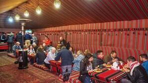 A traditional restaurant with striped red and white walls, wooden ceiling, and hanging lights. Tables are arranged for groups to dine together. - Mohammed Mutlak Camp (Wadi Rum)