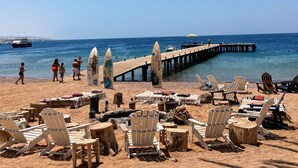 A beach with wooden chairs and a pier extending into the water. - Mohammed Mutlak Camp (Wadi Rum)