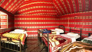A room with four beds, each with a patterned bedspread. The room has a curved ceiling with a red and beige pattern. There is a window on the left wall.