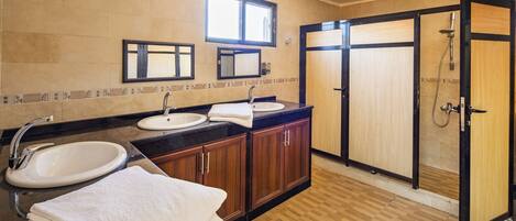 A modern bathroom with two sinks, a large mirror, and a walk-in shower.