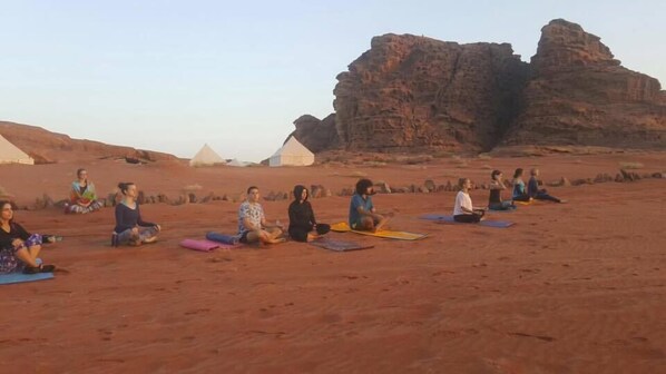 A group of people sitting on mats in a desert setting with rock formations in the background. - Mohammed Mutlak Camp (Wadi Rum)