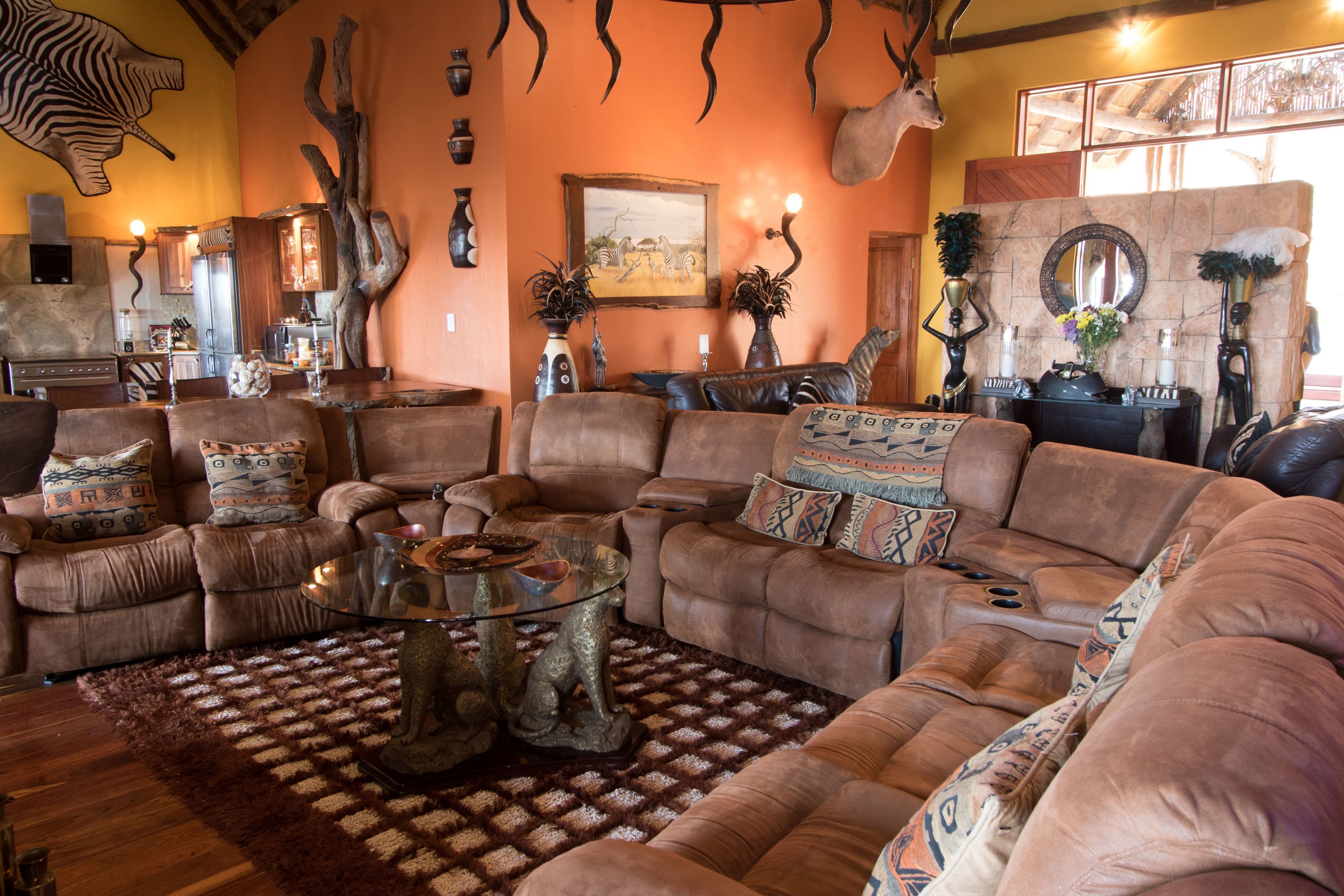 A spacious living room with leather sofas, a glass coffee table, and decorative items including a zebra wall art and antlers.