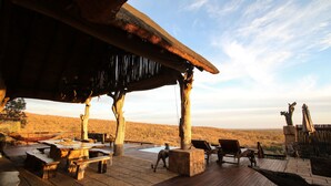 A wooden deck with outdoor furniture, a pool, and a view of the desert landscape. - Phumelelo Lodge (Bela-Bela)