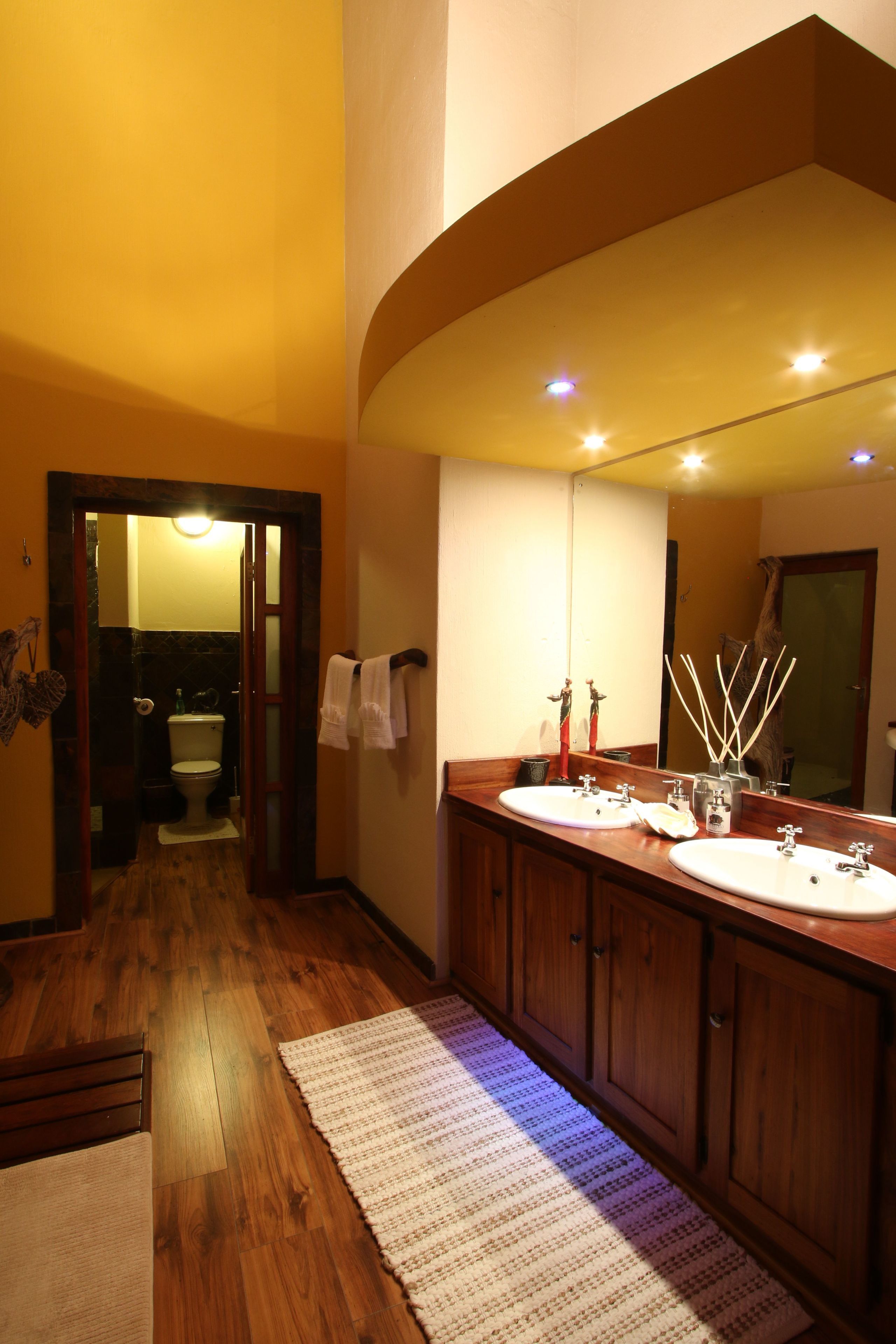 A bathroom with wooden flooring, a large mirror, and two sinks.