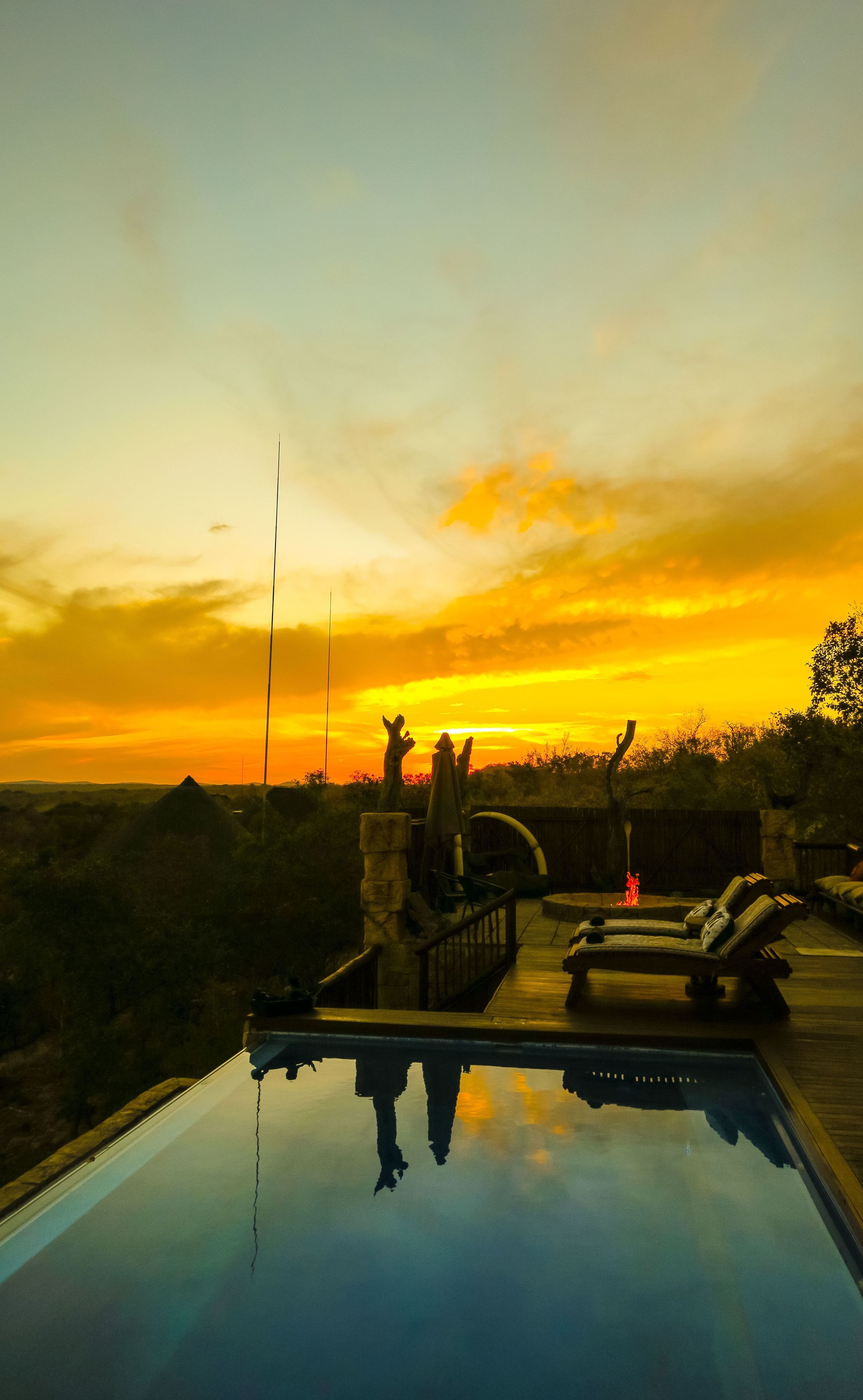 Une piscine avec vue sur le coucher de soleil, une terrasse en bois et des chaises longues.