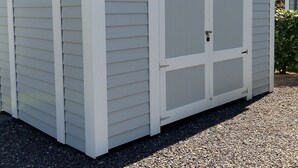 A shed with a white exterior and a grey roof, featuring two large doors and a small window. - Villa Regina (Moehnesee)